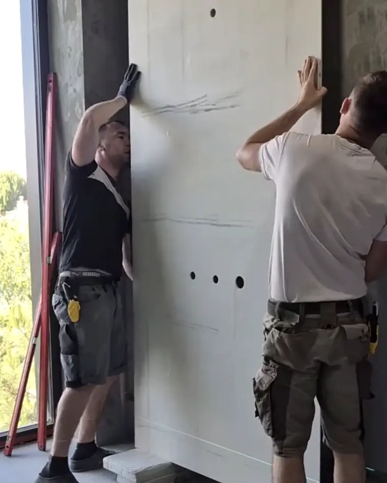 Zwei Handwerker stellen eine grossformatige Keramikplatte an der Wand auf